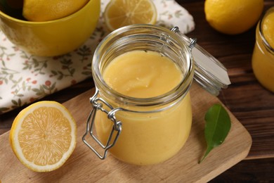 Photo of Delicious lemon curd in glass jars, fresh citrus fruits and green leaf on wooden table