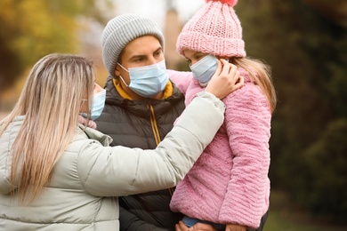 Photo of Family in medical masks outdoors on autumn day. Protective measures during coronavirus quarantine