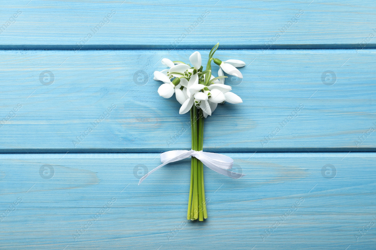 Photo of Beautiful bouquet of snowdrops on light blue wooden table, top view