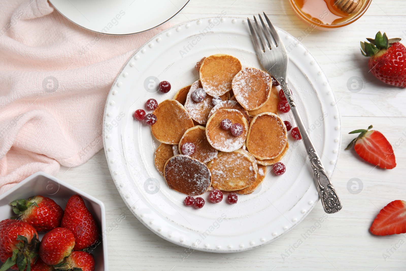 Photo of Delicious mini pancakes cereal with cranberries served on white wooden table, flat lay