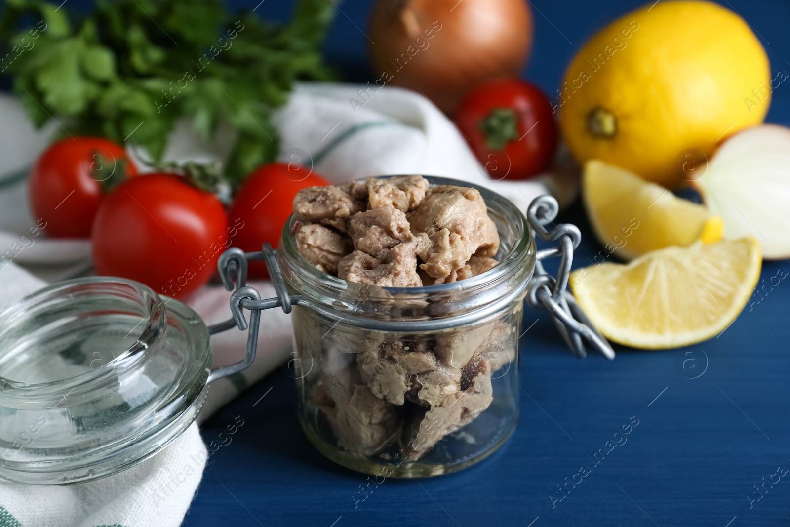 Photo of Glass jar of tasty cod liver and different products on blue wooden table