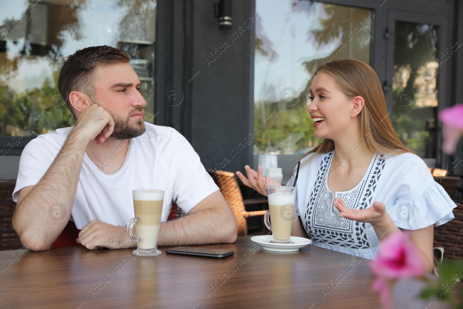 Photo of Young man having boring date with talkative girl in outdoor cafe