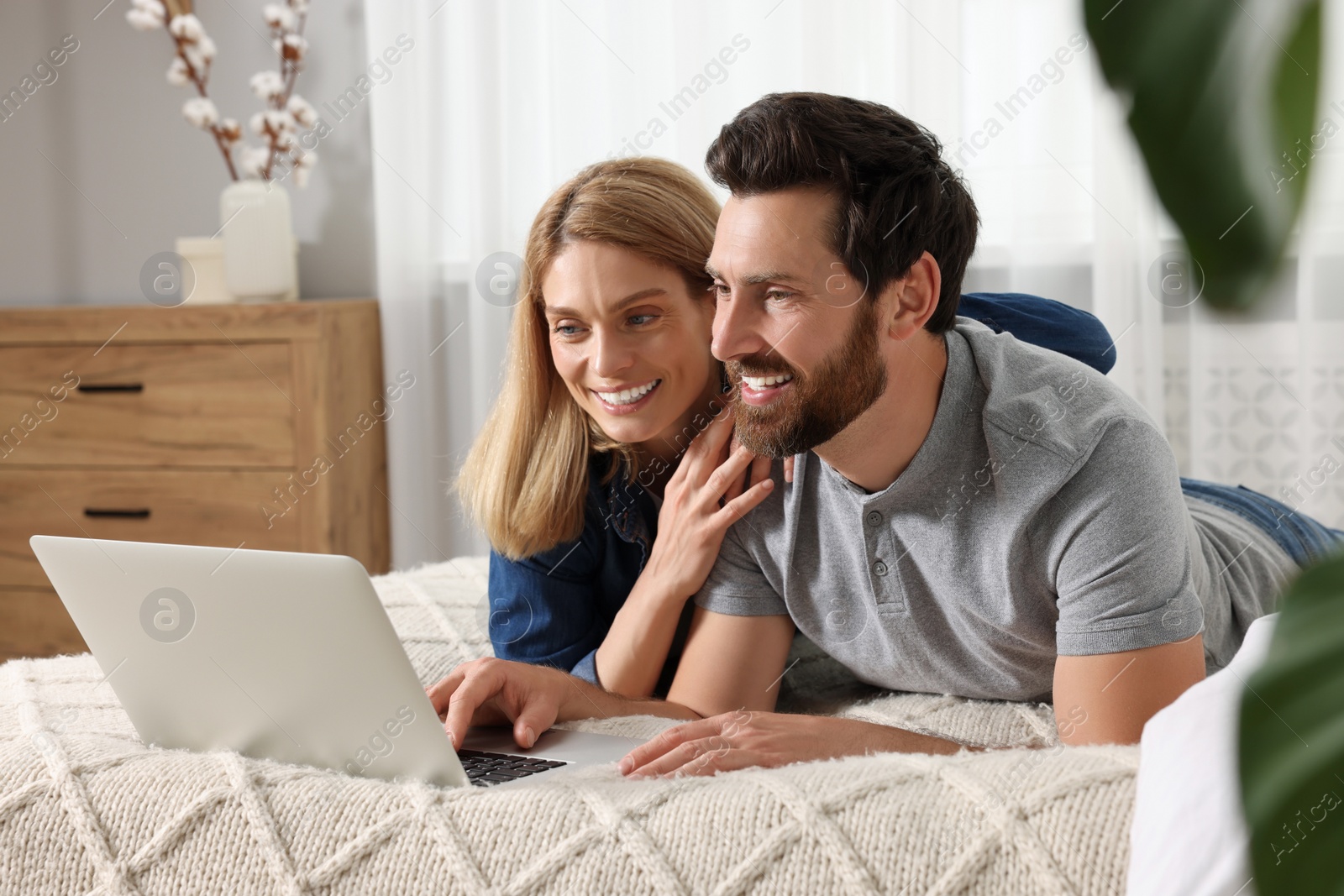 Photo of Happy couple with laptop on bed at home