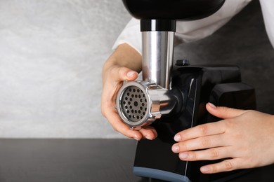 Photo of Woman assembling electric meat grinder at black table, closeup. Space for text