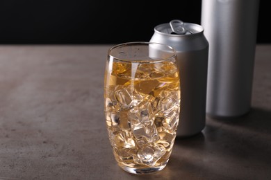 Energy drink with ice cubes in glass and aluminium cans on grey table, closeup