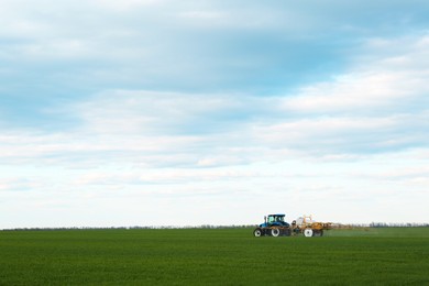 Photo of Tractor spraying pesticide in field on spring day. Agricultural industry