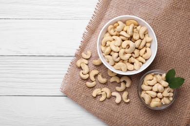 Photo of Tasty cashew nuts and green leaves on white wooden table, flat lay. Space for text