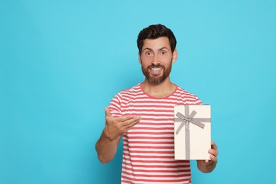 Handsome man holding gift box on turquoise background, space for text