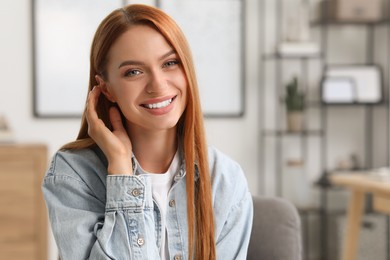 Photo of Portrait of beautiful young woman with red hair at home. Attractive lady smiling and looking into camera. Space for text