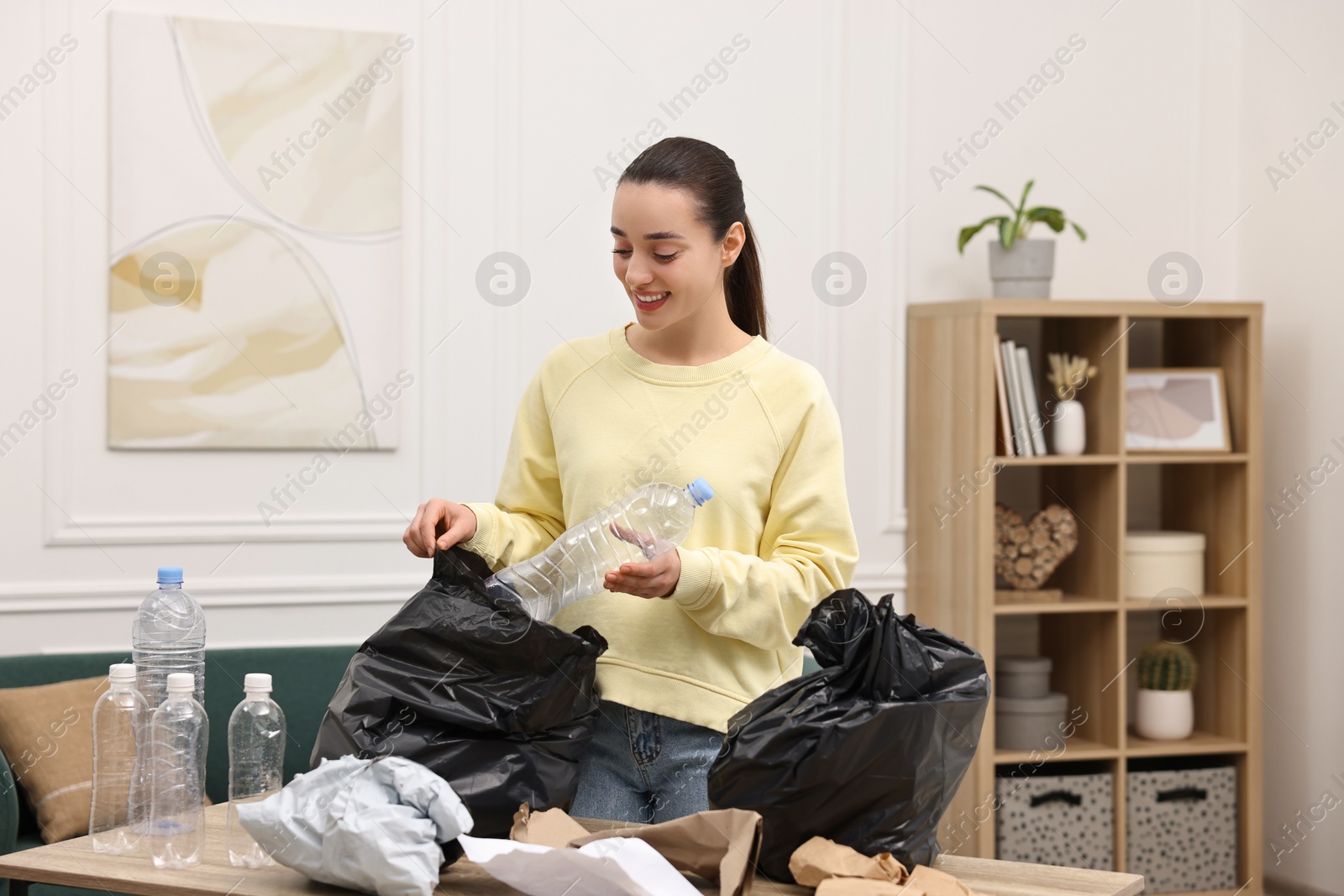 Photo of Smiling woman with plastic bag separating garbage in room