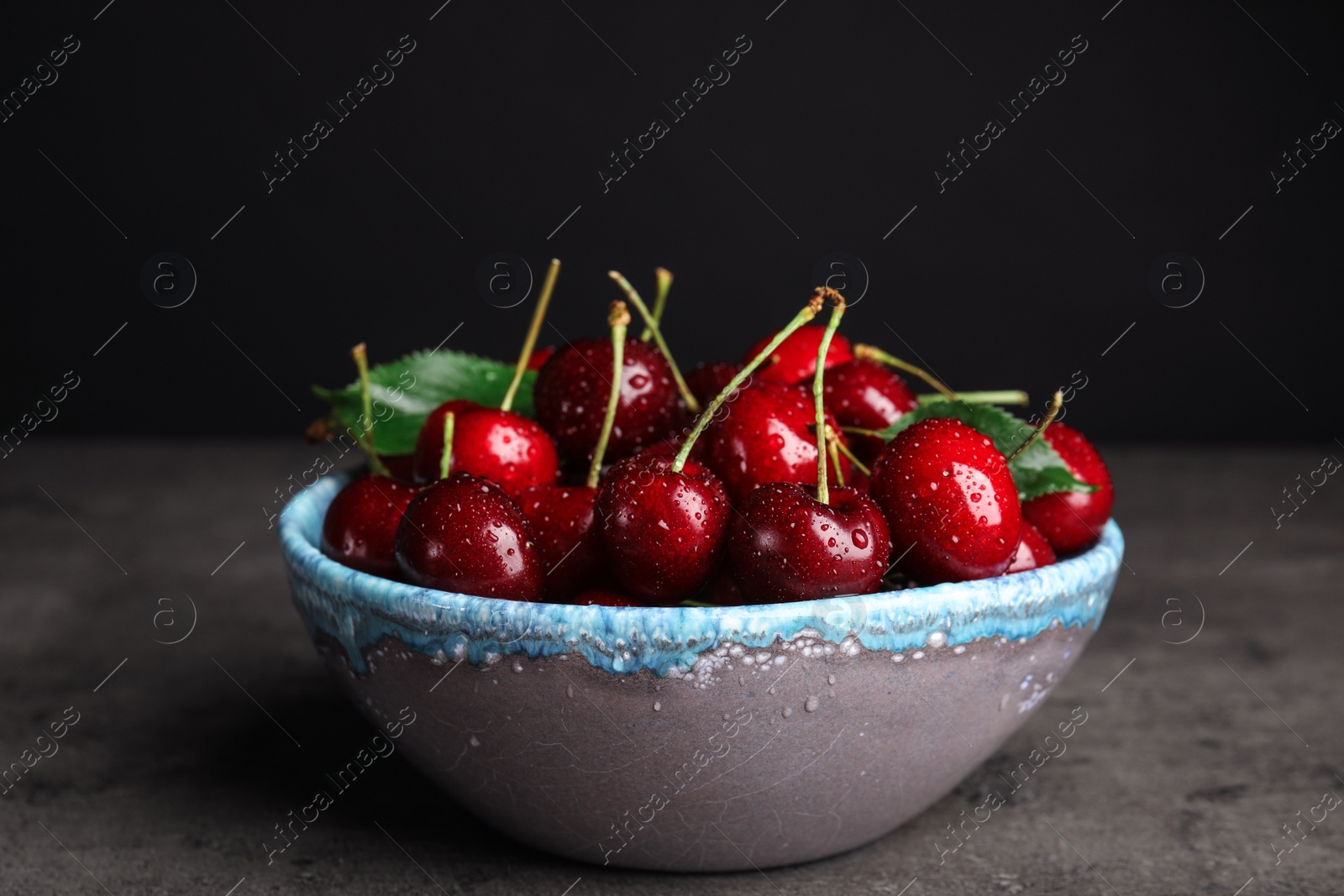 Photo of Bowl with delicious sweet cherries on grey table