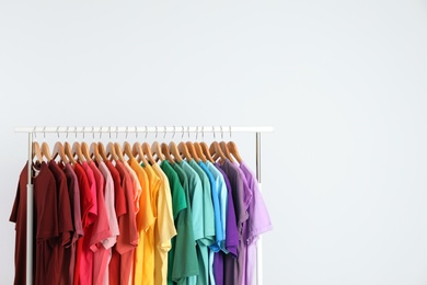 Photo of Rack with rainbow clothes on light background