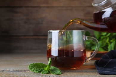 Pouring hot aromatic mint tea into cup on wooden table, space for text