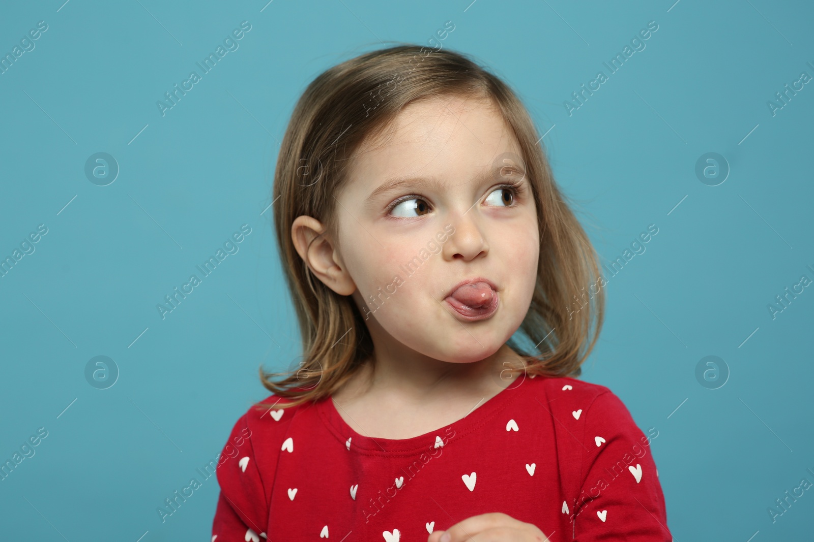 Photo of Funny little girl showing her tongue on light blue background