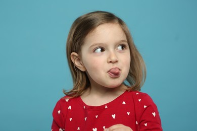 Photo of Funny little girl showing her tongue on light blue background