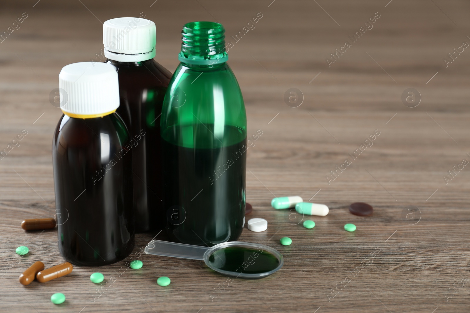 Photo of Bottles of cough syrup, dosing spoon and pills on wooden table