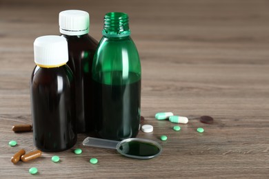 Photo of Bottles of cough syrup, dosing spoon and pills on wooden table