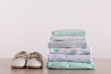 Photo of Stack of baby boy's clothes and shoes on wooden table against white background, space for text