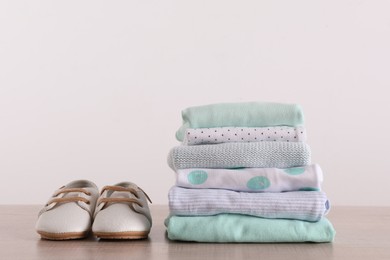 Stack of baby boy's clothes and shoes on wooden table against white background, space for text