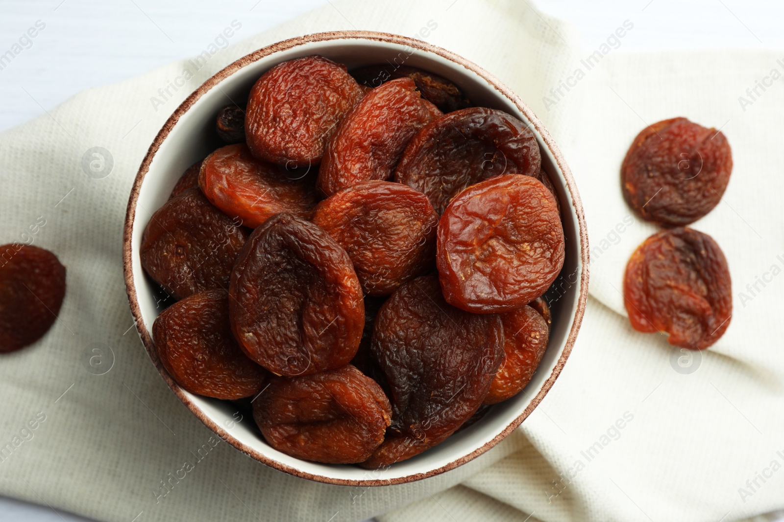 Photo of Bowl of tasty apricots and napkin on table, top view. Dried fruits