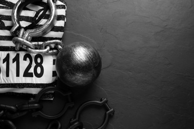 Photo of Prisoner ball with chain and jail clothes on black table, flat lay. Space for text