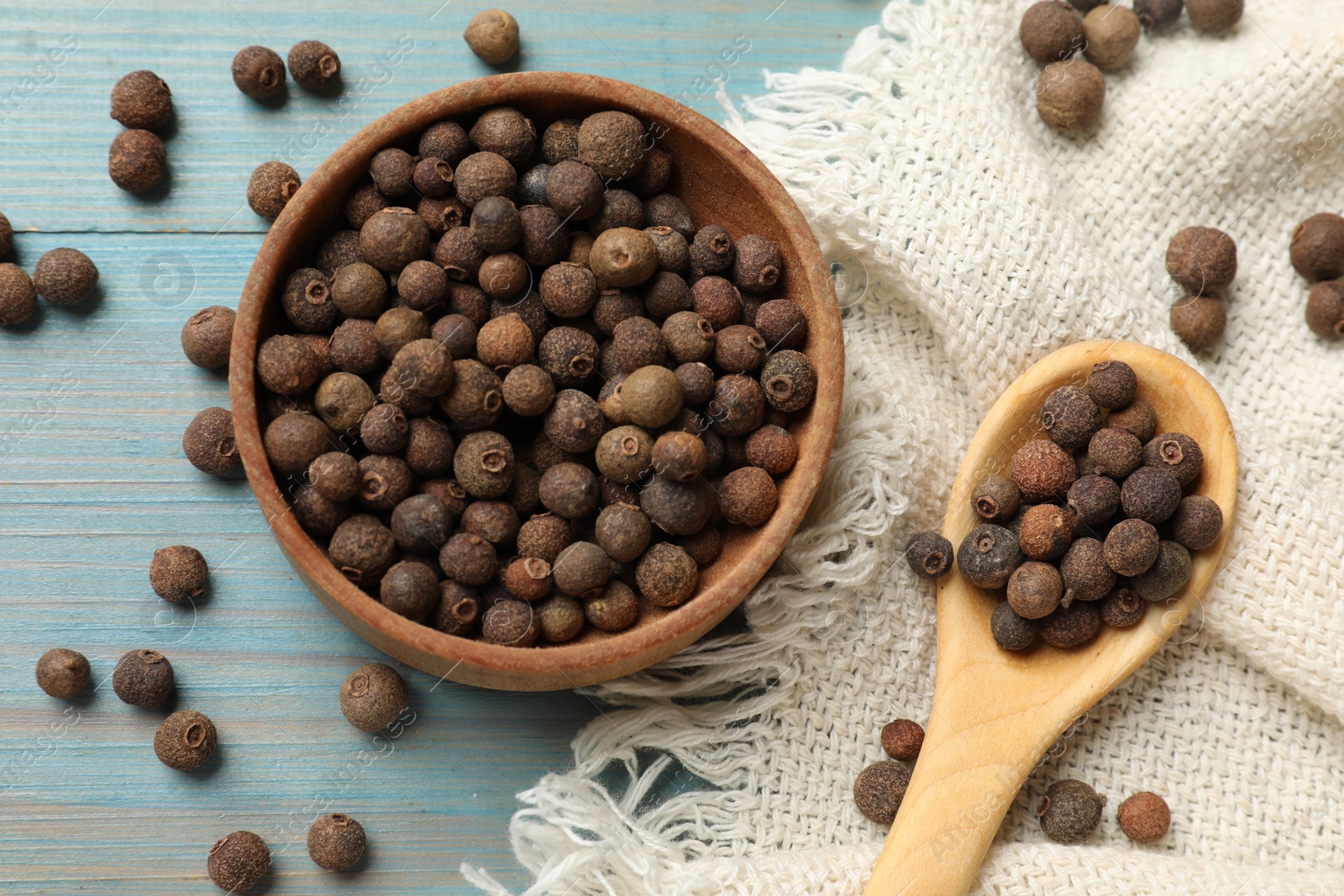 Photo of Aromatic allspice pepper grains in bowl and spoon on light blue wooden table, top view