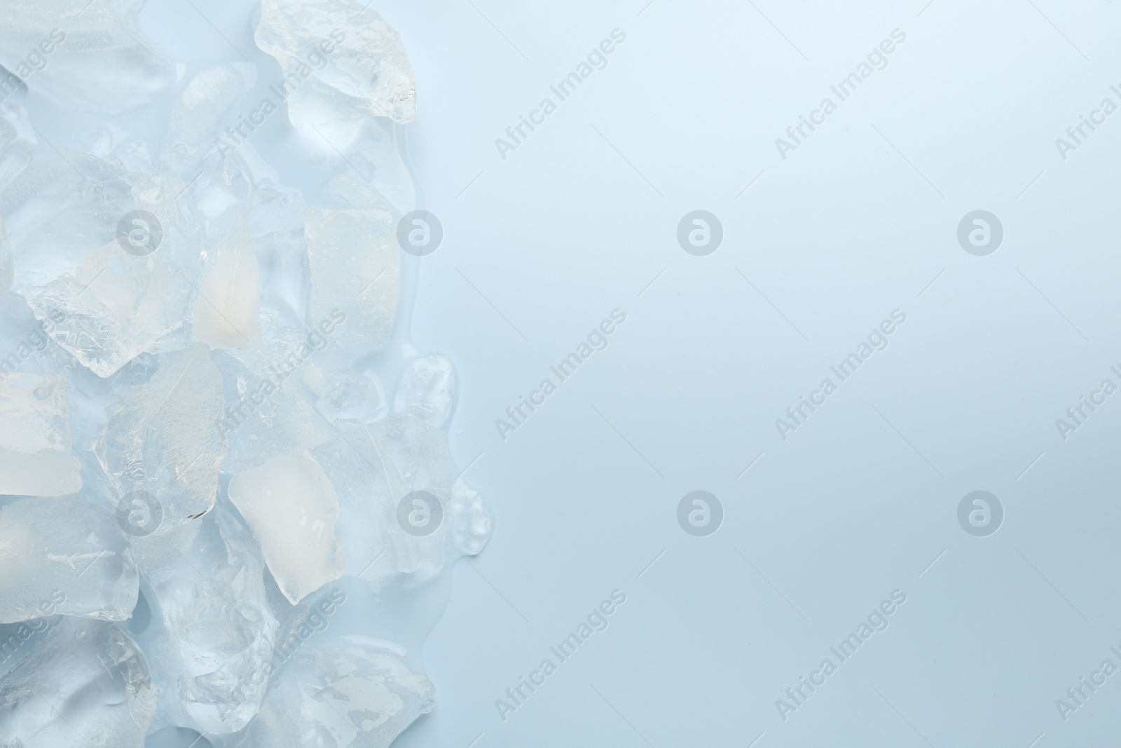 Photo of Pieces of crushed ice on light blue background, top view. Space for text