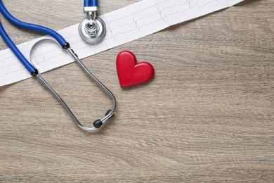 Photo of Cardiogram report, red heart and stethoscope on wooden table, flat lay. Space for text
