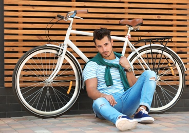 Handsome young hipster man with bicycle near wooden wall outdoors