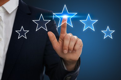 Image of Quality rating. Man pointing at stars on virtual screen against blue background, closeup