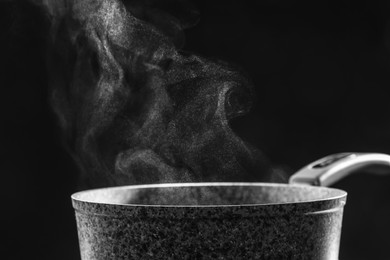 Photo of Steaming saucepan on dark background, closeup. Space for text