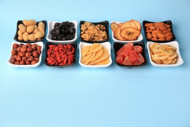 Bowls with dried fruits and nuts on light blue background, space for text