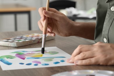 Photo of Woman painting with watercolor at wooden table indoors, closeup