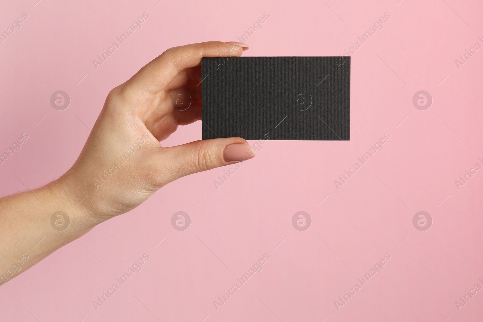 Photo of Woman with blank black business card on pink background, closeup. Mockup for design