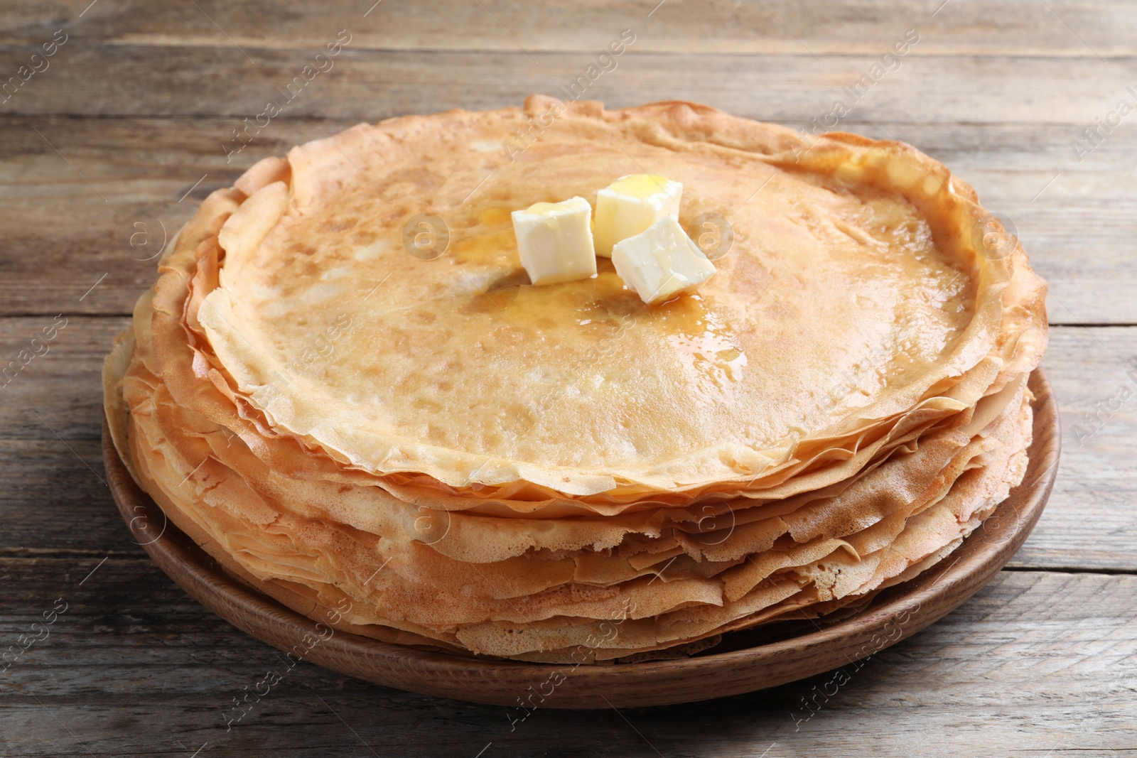 Photo of Stack of delicious crepes with melting butter on wooden table