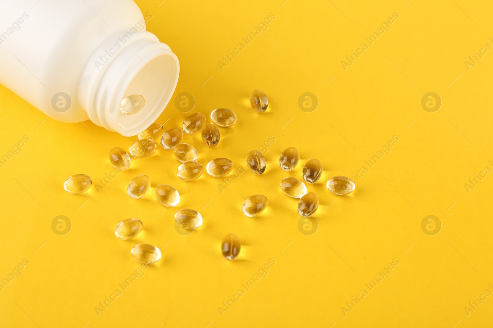 Photo of White medical bottle and vitamin capsules on yellow background, above view. Space for text