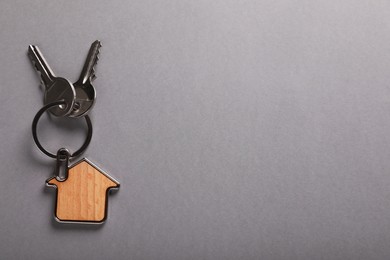 Keys with trinket in shape of house on grey background, top view and space for text. Real estate agent services