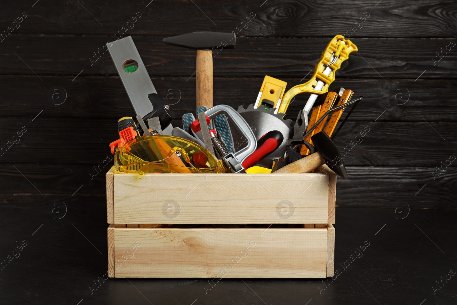 Photo of Wooden crate with different carpenter's tools on black table