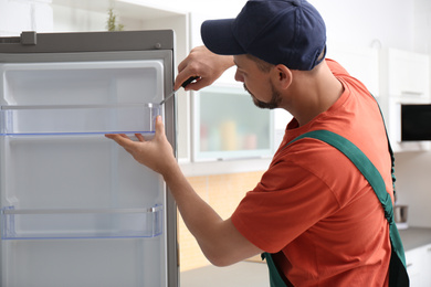 Photo of Male technician with screwdriver repairing refrigerator indoors