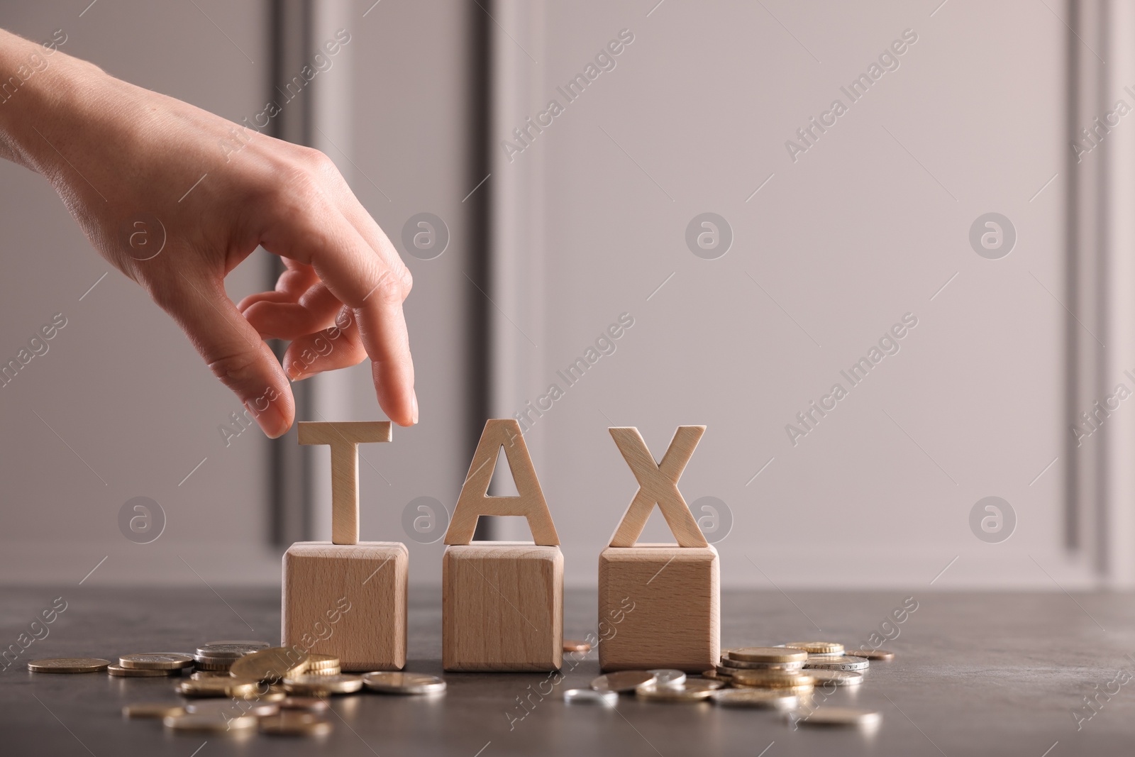 Photo of Woman with word Tax, wooden cubes and coins at grey table, closeup. Space for text