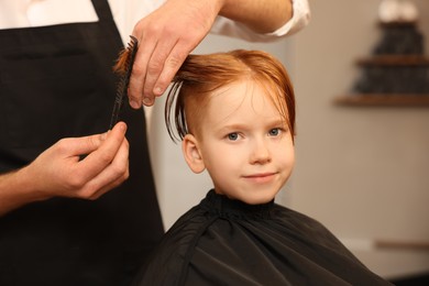 Photo of Professional hairdresser combing boy's hair in beauty salon, closeup
