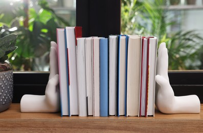 Beautiful hand shaped bookends with books on window sill indoors