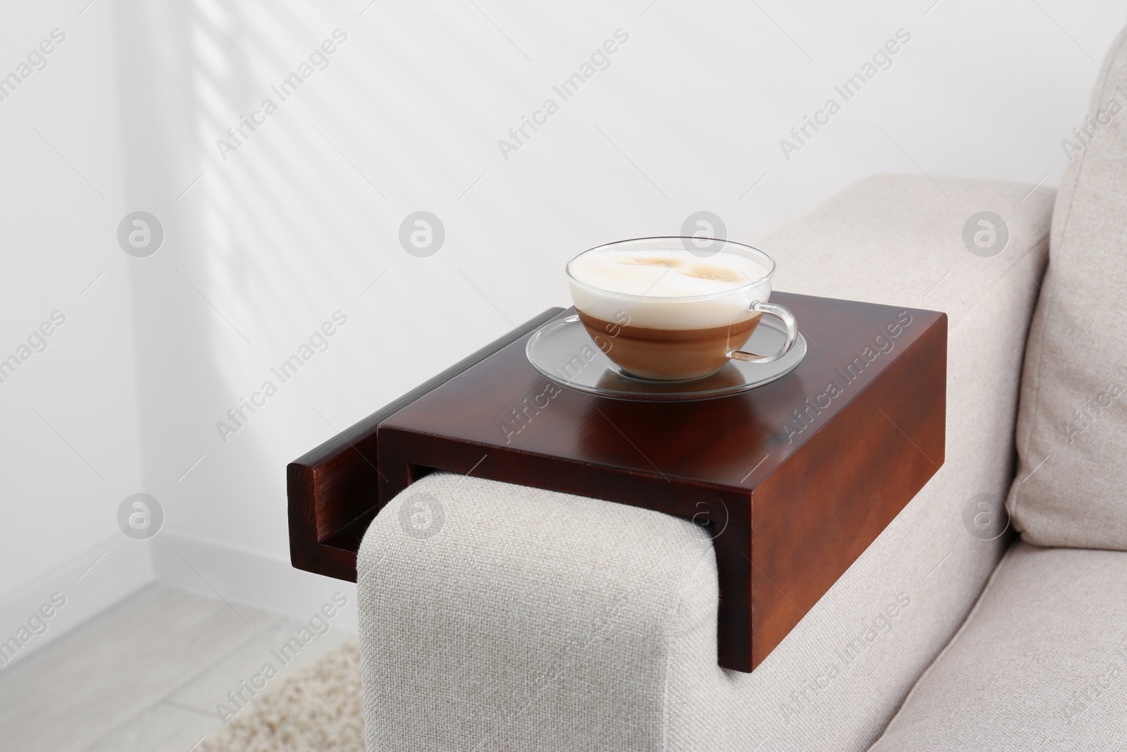 Photo of Cup of coffee on sofa with wooden armrest table indoors. Interior element