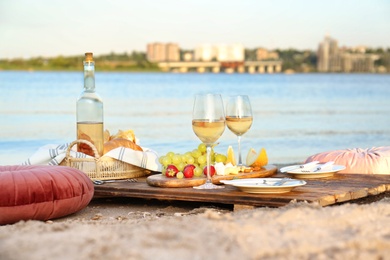 Food for picnic and white wine served on wooden pallet near river