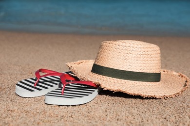 Striped flip flops and straw hat on sandy beach near sea