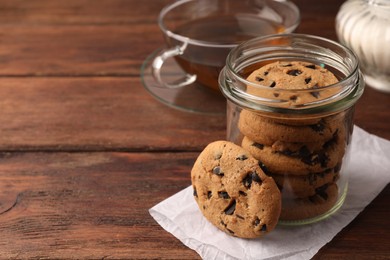 Photo of Glass jar with delicious chocolate chip cookies and tea on wooden table. Space for text