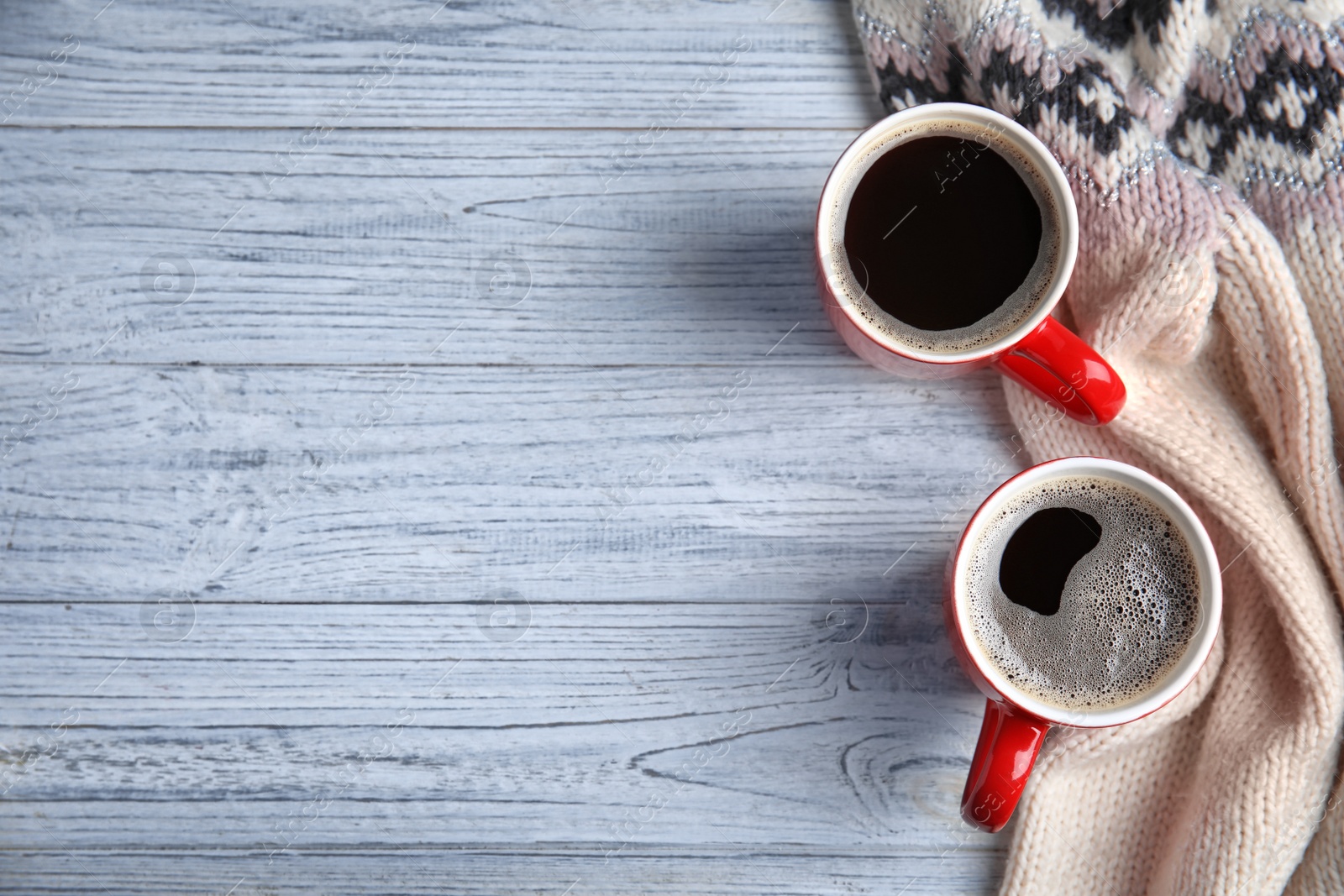 Photo of Flat lay composition cups of hot coffee and knitted sweater on light wooden background, space for text. Winter drink