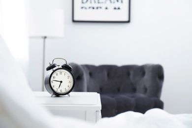 Photo of Analog alarm clock on table in bedroom. Time of day