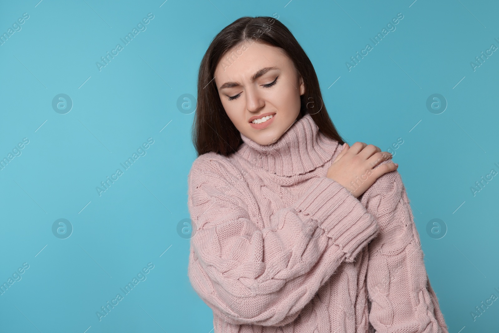 Photo of Young woman suffering from pain in her shoulder on light blue background, space for text. Arthritis symptoms