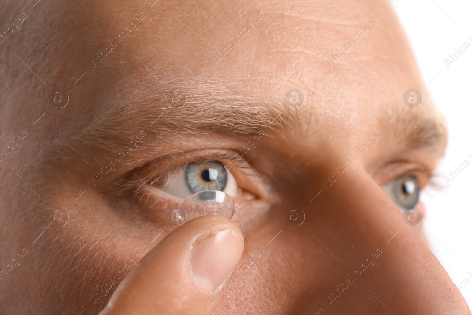 Photo of Young man putting contact lens into his eye, closeup